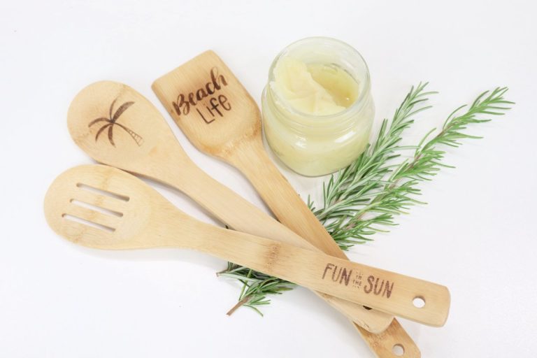 Image contains a jar of wood butter, three decorative wooden utensils, and rosemary.