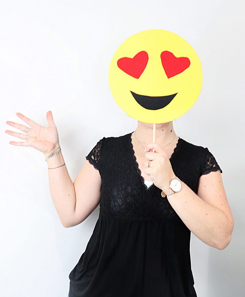 Image contains a woman holding up an emoji mask.