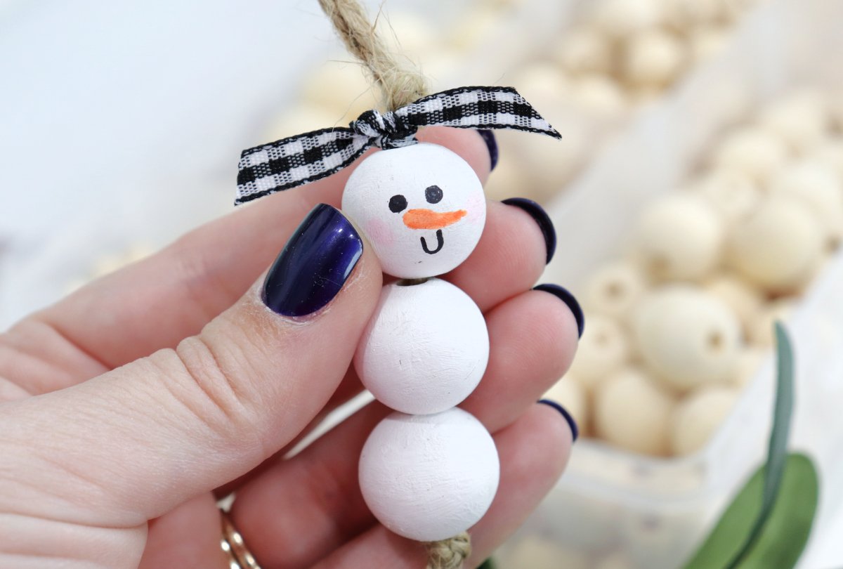 Image contains a hand holding a beaded snowman ornament.