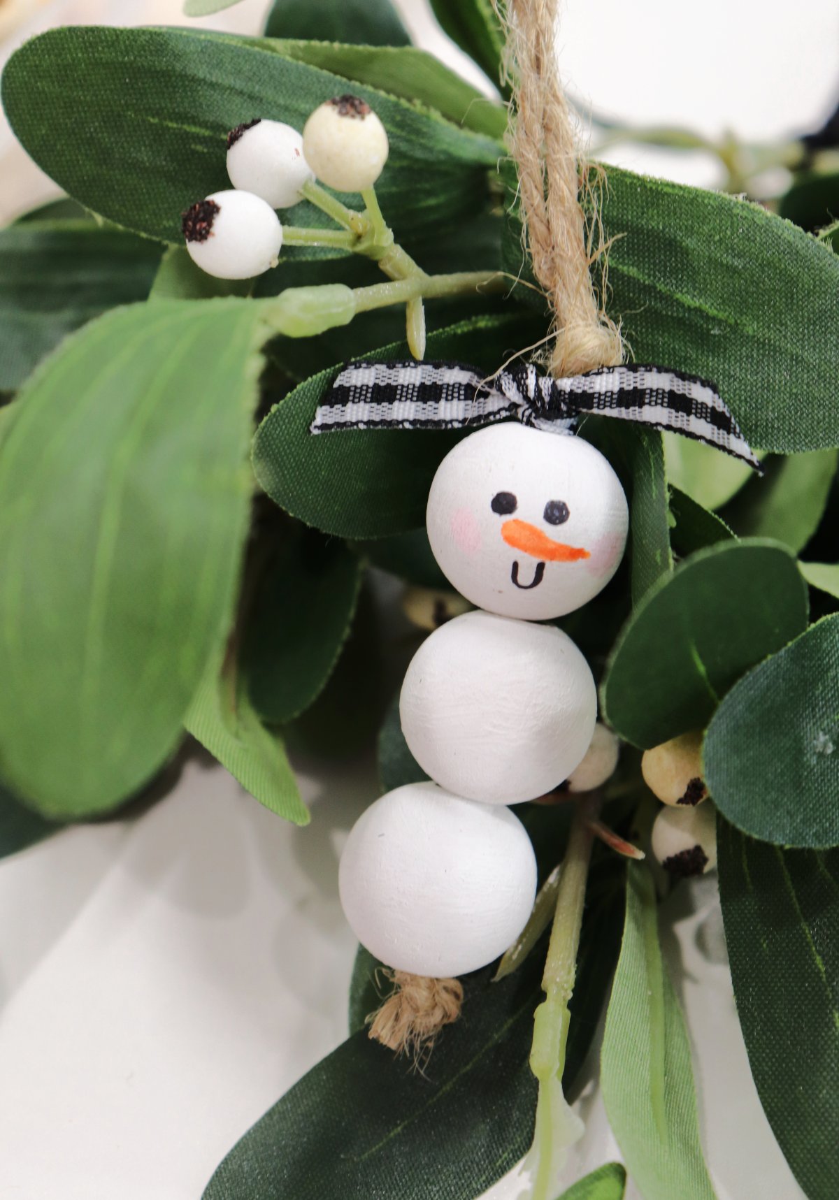 This image contains a white beaded snowman ornament with a ribbon tie and mistletoe.
