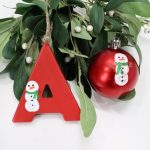 Image contains two red ornaments with white snowmen on them, and mistletoe.