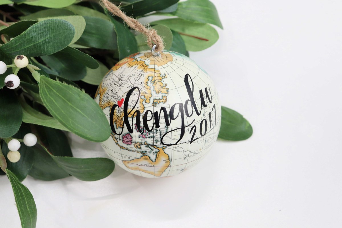 Image contains a cream colored globe ornament with the words "Chengdu 2017" lettered on it, and mistletoe.