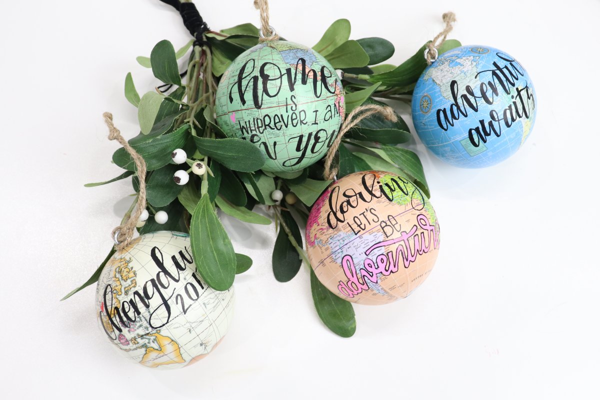 Image contains four hand lettered globe ornaments and mistletoe.
