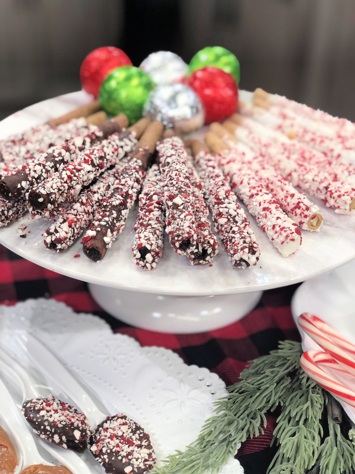 Image contains chocolate dipped pirouette cookies rolled in peppermint, and hot cocoa bombs on a white plate.