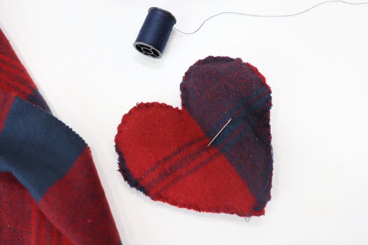 Image contains a fabric plush heart made of red and blue plaid fleece, and a spool of blue thread.