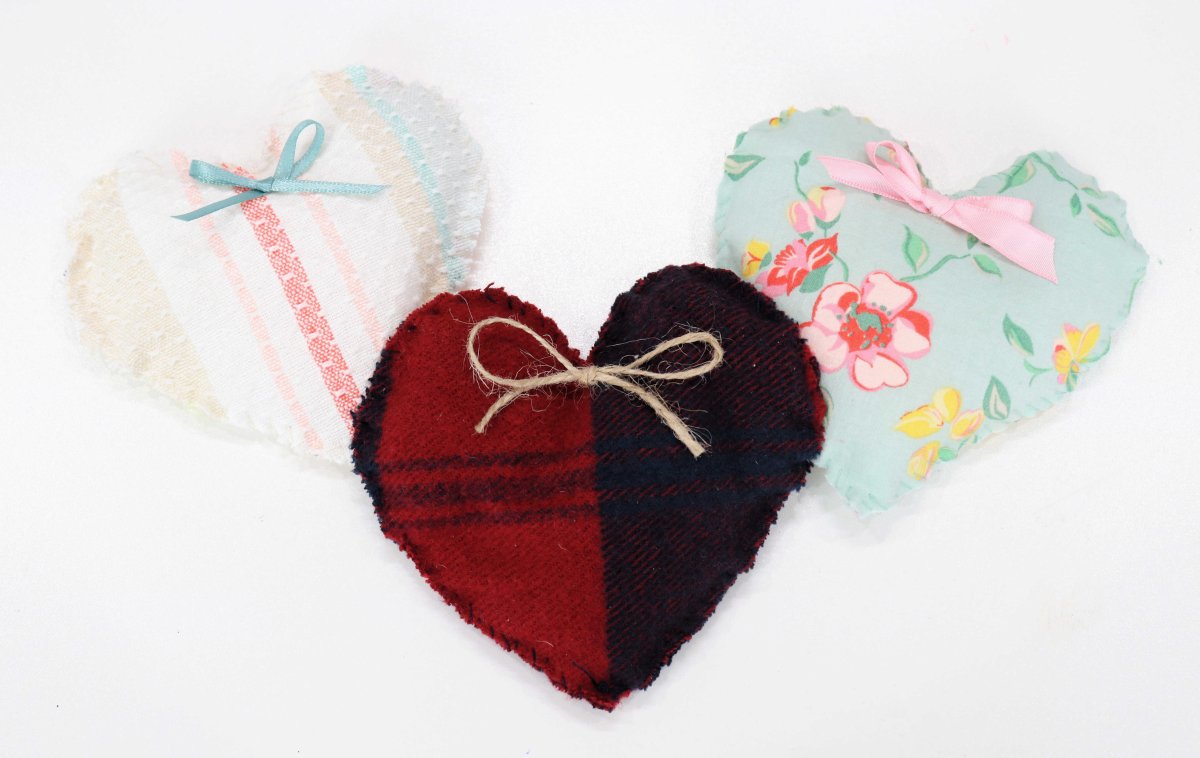 Image contains three plush fabric hearts; one with multicolored stripes, one with red and navy plaid, and one green with pink and yellow flowers.