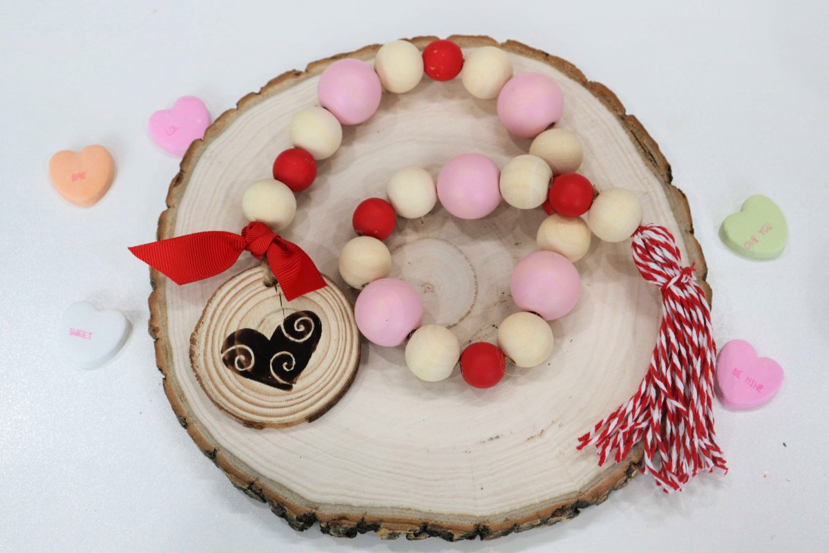 Image contains a wooden bead garland on top of a large wood slice, surrounded by colored candy hearts.