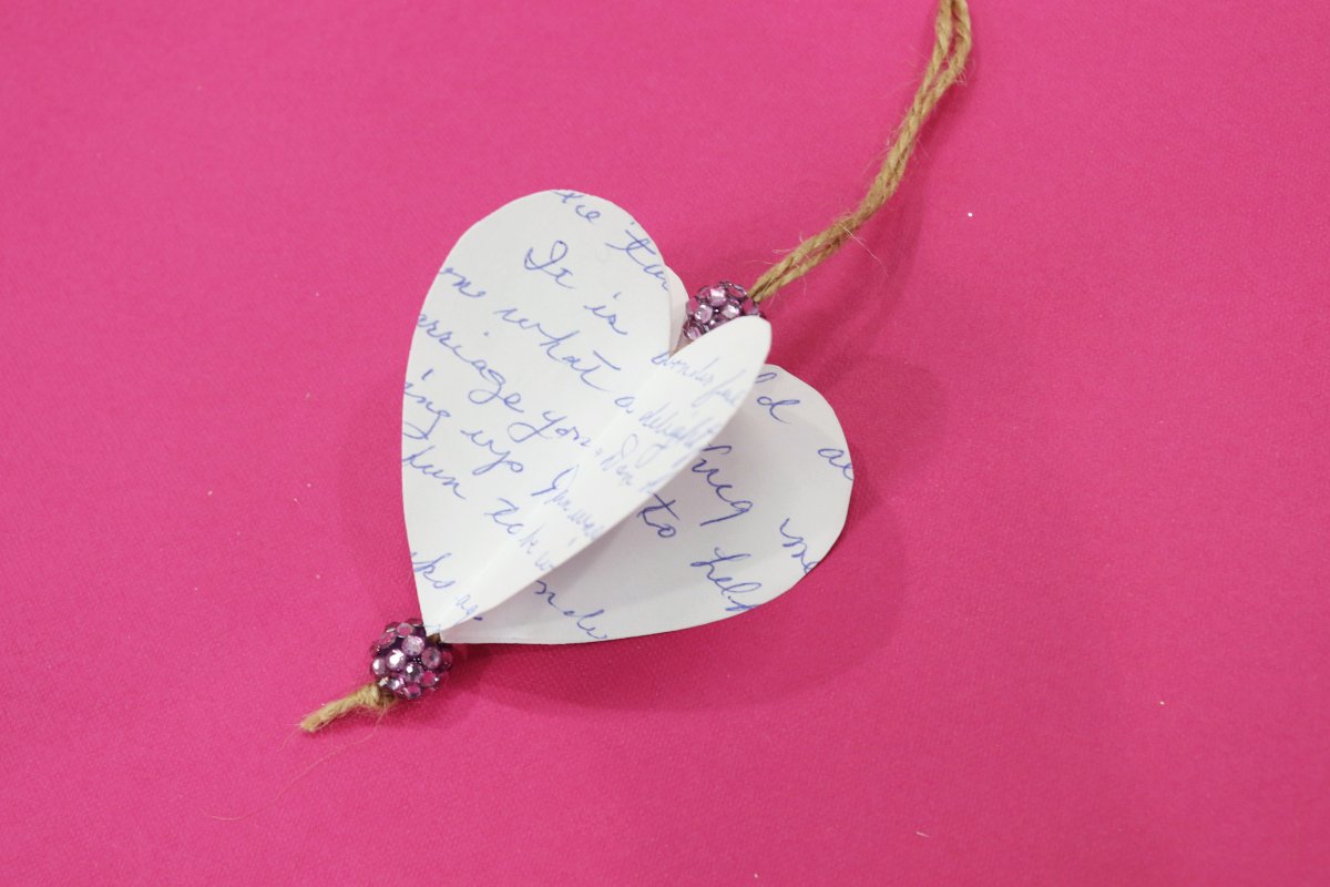 Image contains a three-dimensional paper heart made from a handwritten note on a pink background.