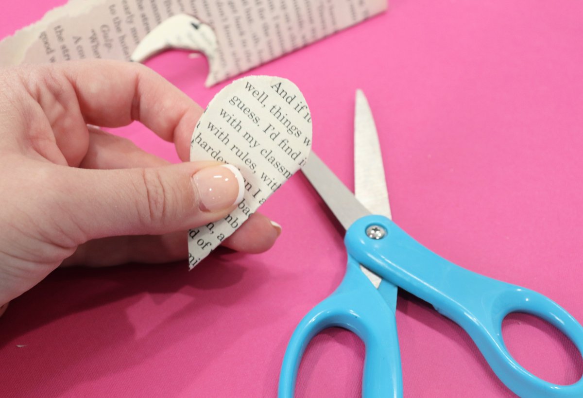 Image contains a pair of scissors and a hand holding hearts cut from book pages on a pink background.