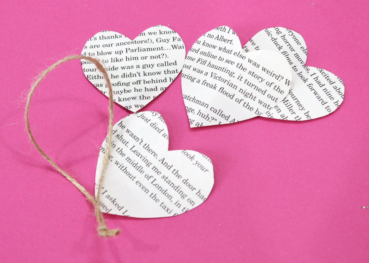 Image contains four heart shapes cut from book pages and a piece of jute on a pink background.