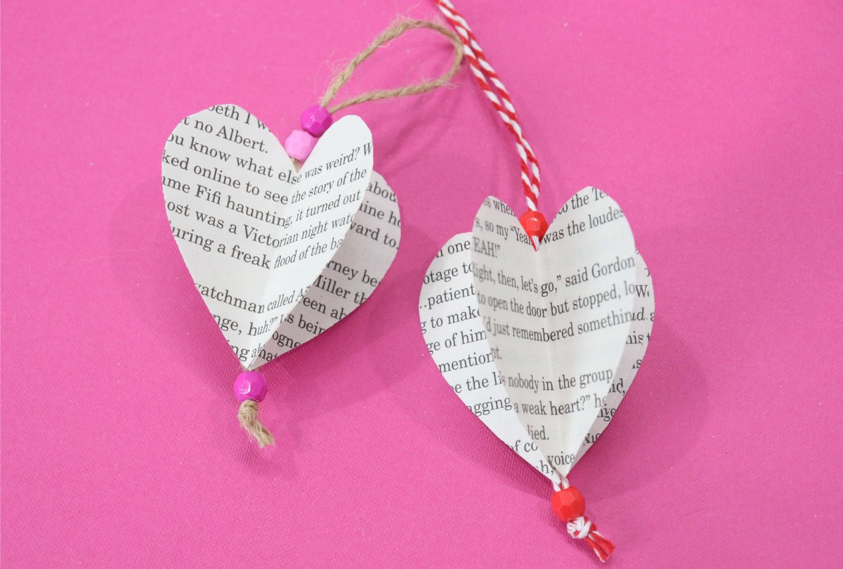 Image contains two three-dimensional paper hearts made from book pages on a pink background.