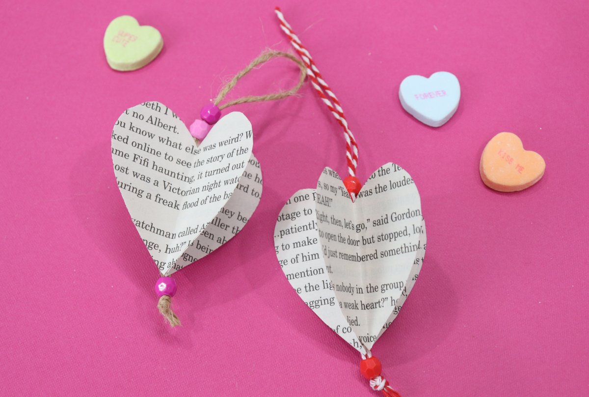 Image contains two three-dimensional paper hearts on a pink background surrounded by candy hearts.