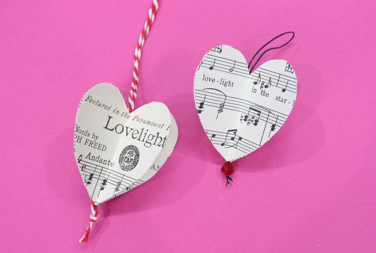 Image contains two paper hearts made from sheet music, on a pink background.