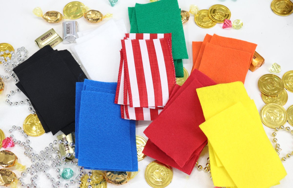 This image contains felt rectangles in a variety of colors on a white background with gold wrapped candies, plastic gems, and plastic beads.