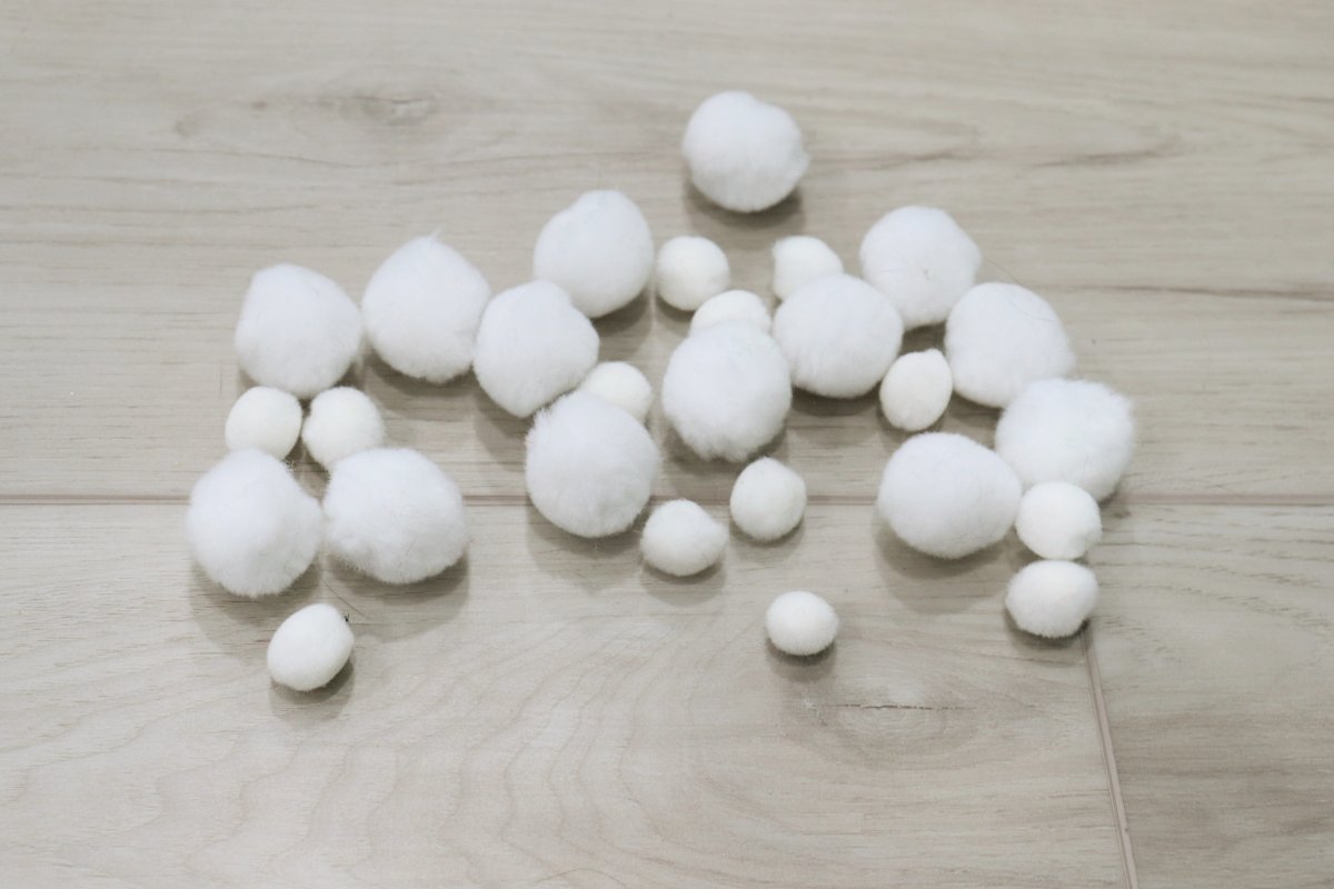 Image contains a pile of white pom poms in assorted sizes.