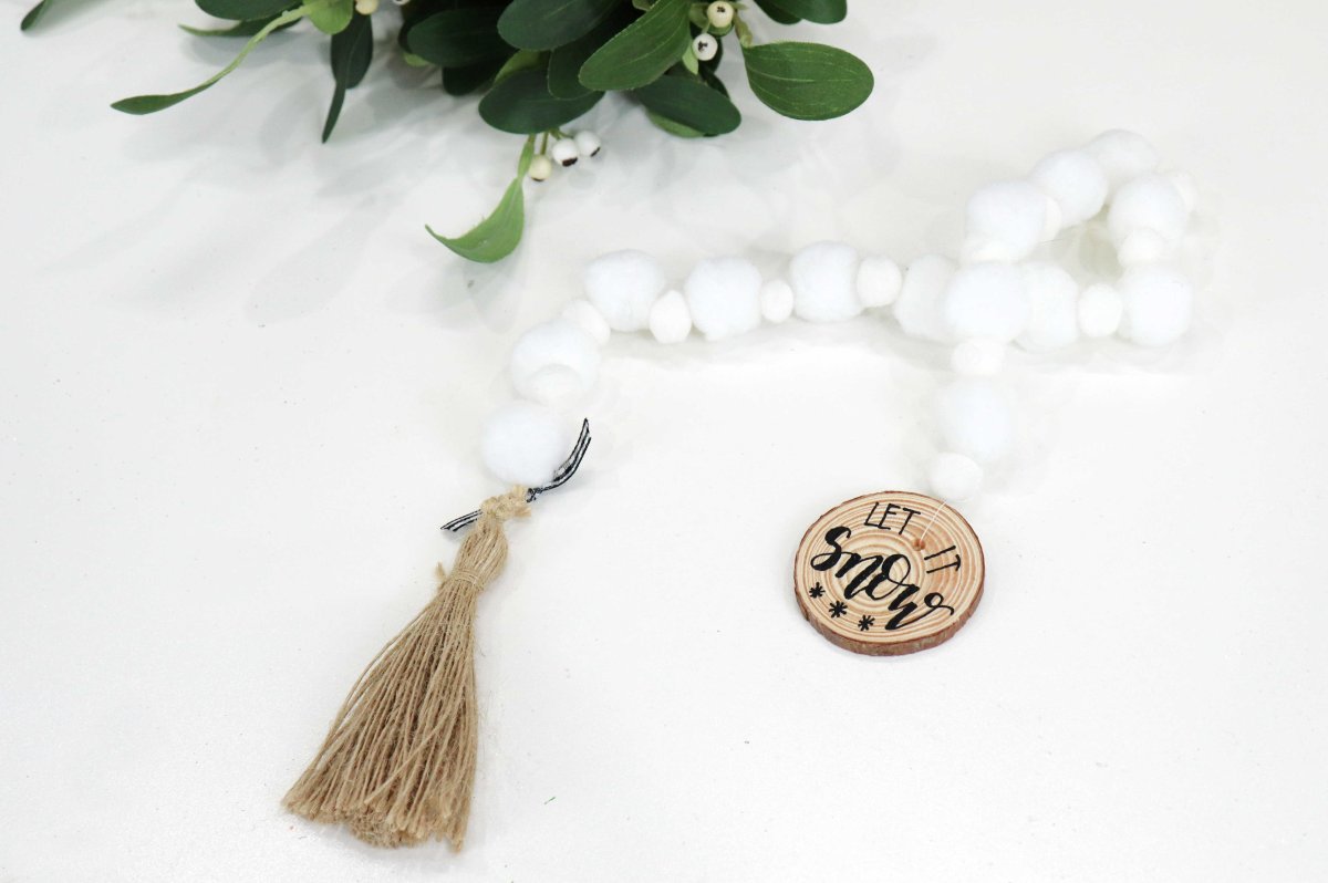 Image contains a snowball garland with a tassel on the end, and mistletoe.
