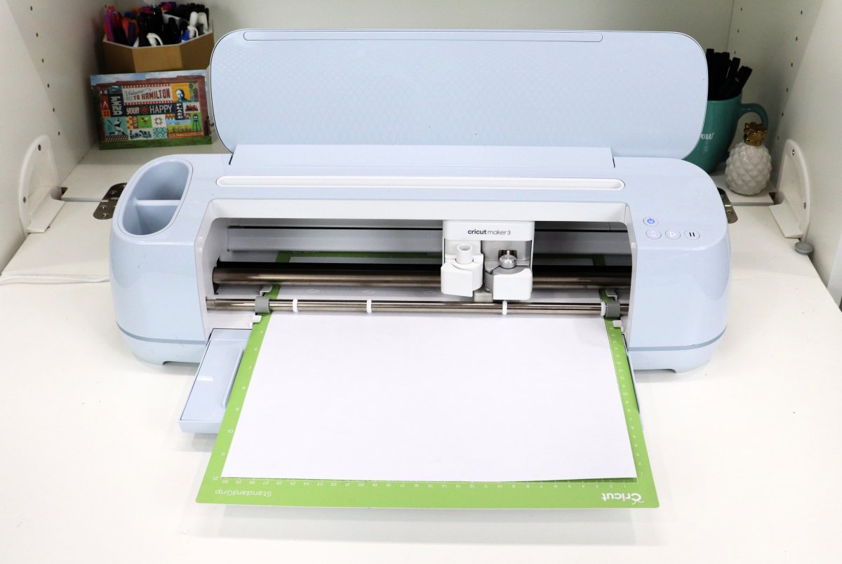 Image contains a Cricut Maker 3 cutting white cardstock.