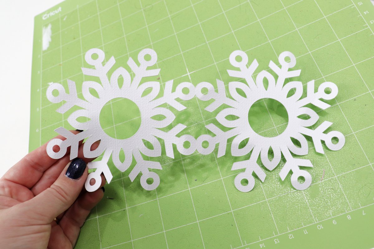 Image contains a hand holding snowflakes cut from white cardstock.