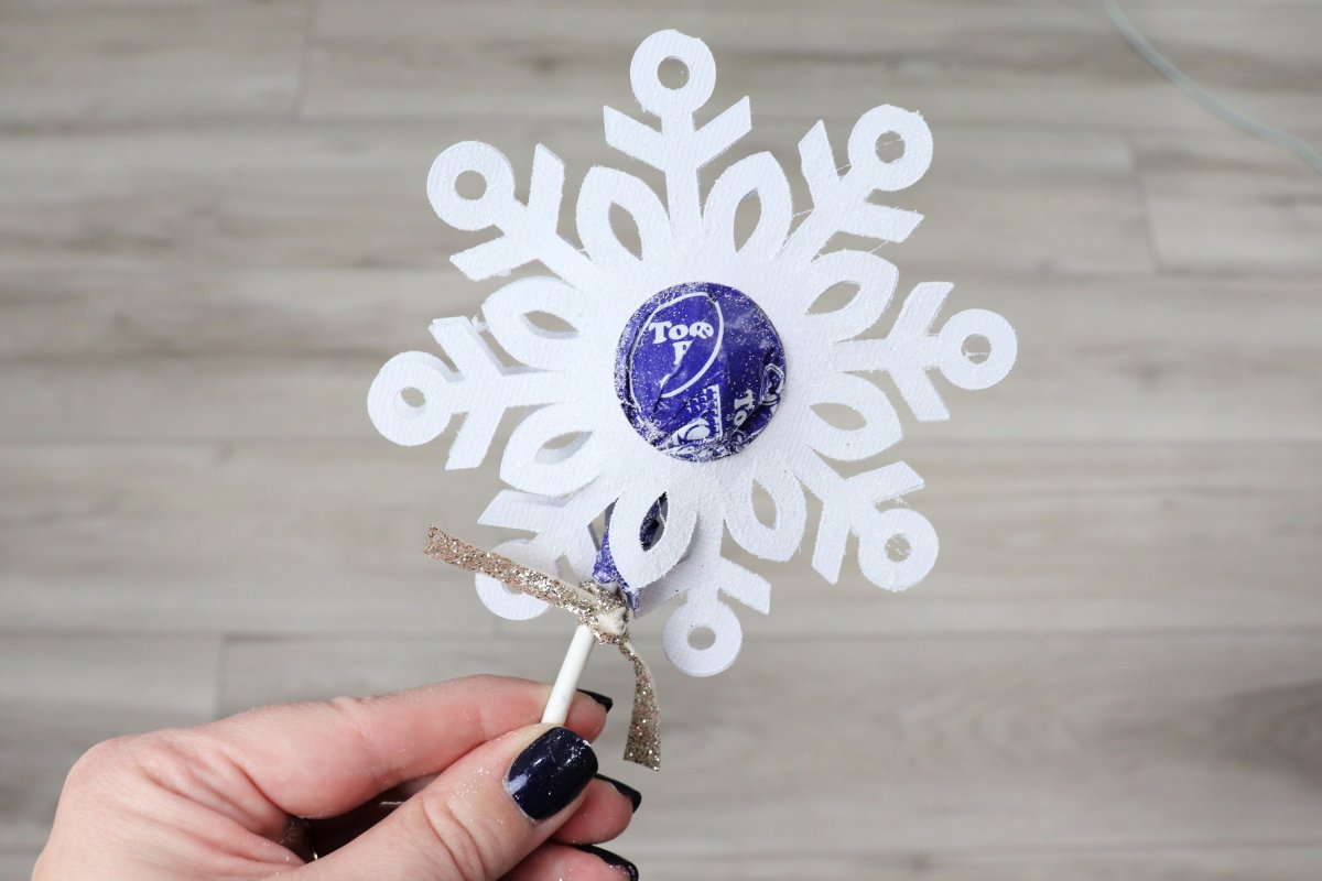 Image contains a hand holding a lollipop decorated with a snowflake border.