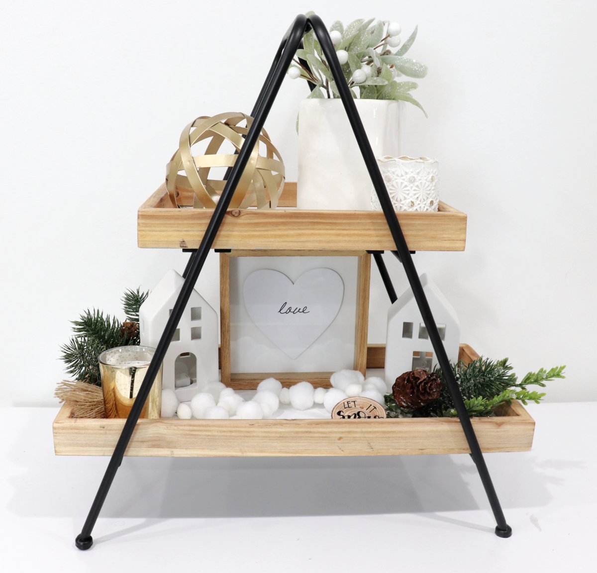 Image contains a two-tiered tray decorated for winter with neutral colors and greenery.