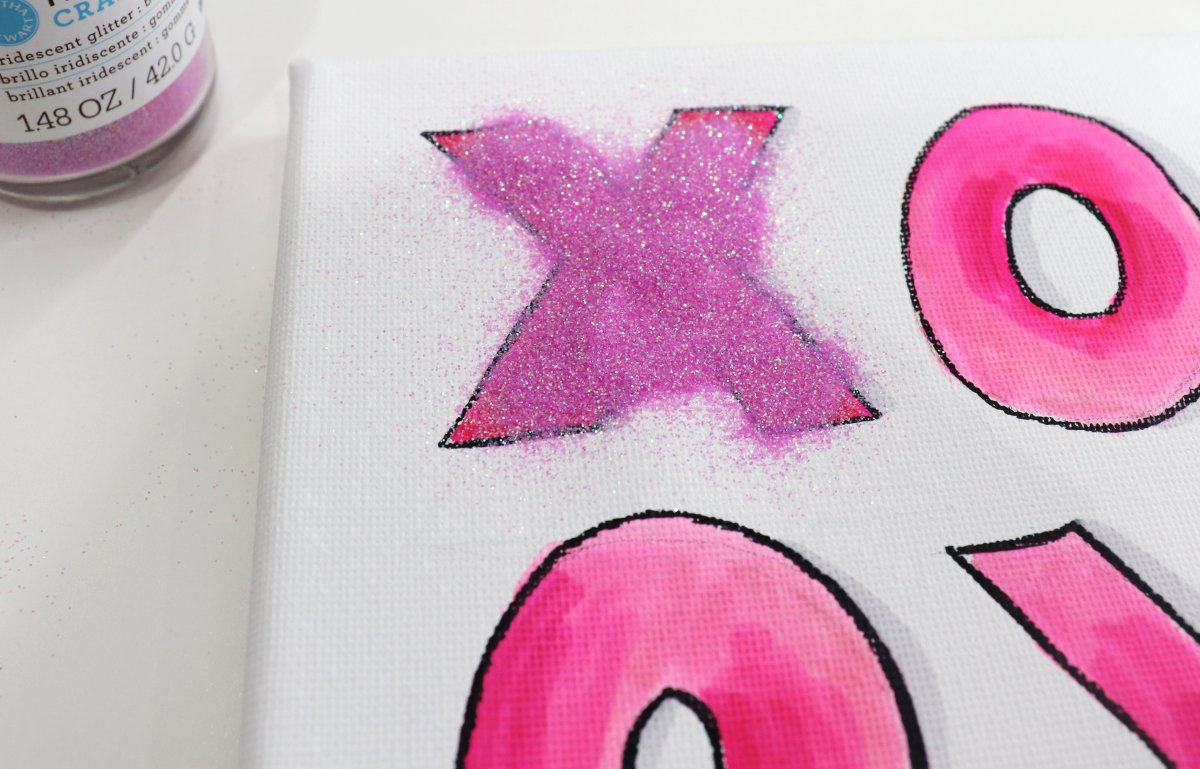 Image contains marker drawn letters on canvas, one covered with pink glitter.