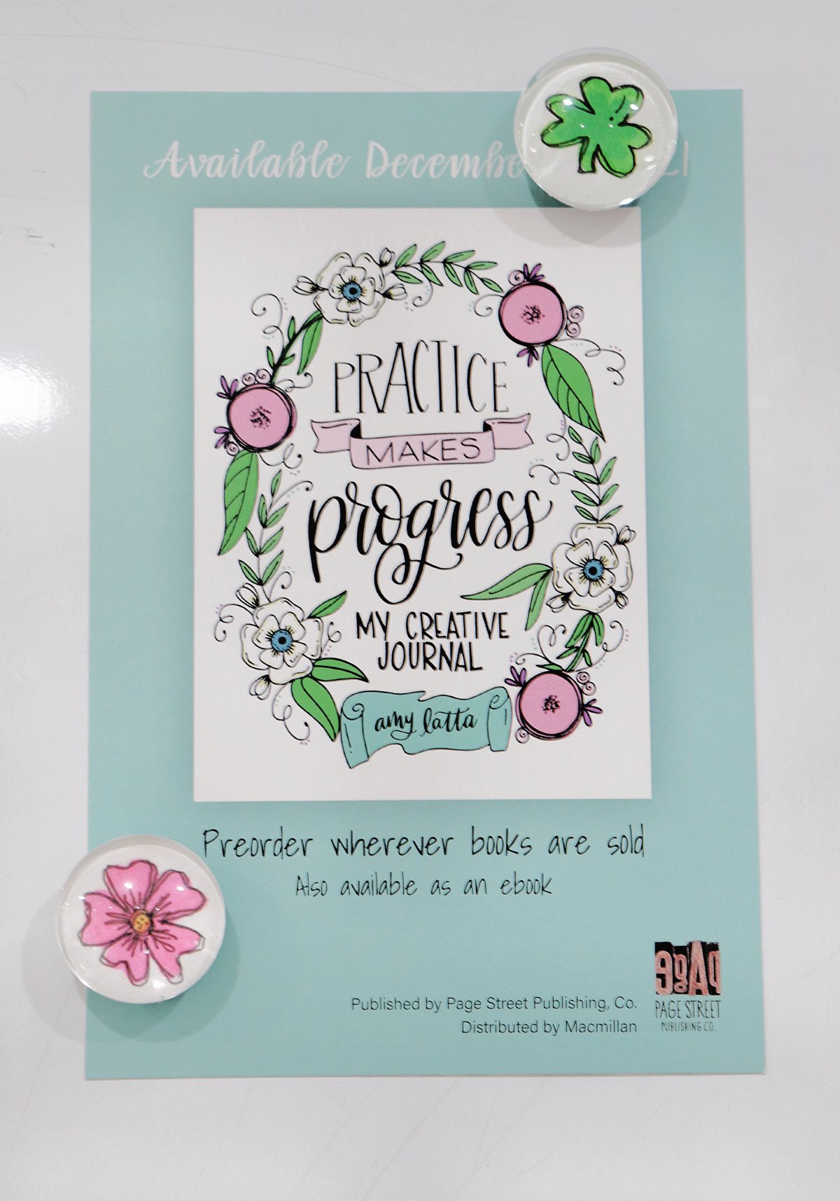 Image contains a teal promotional flyer for the new book Practice Makes Progress, attached to a white board with two handmade magnets. One magnet features a green shamrock and the other features a pink hand-drawn flower.