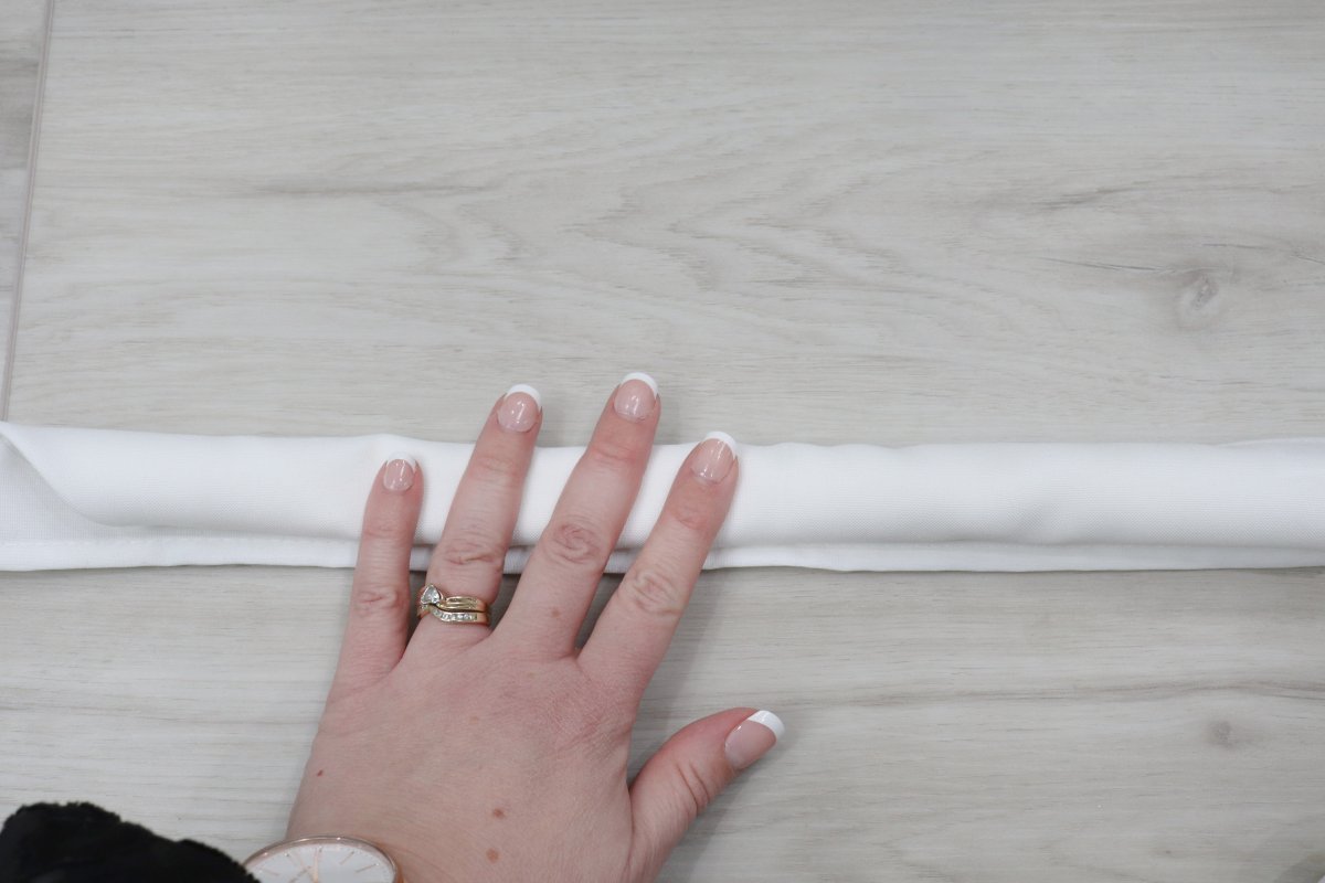 Image shows Amy's hand rolling a white cloth napkin on top of a wooden background.