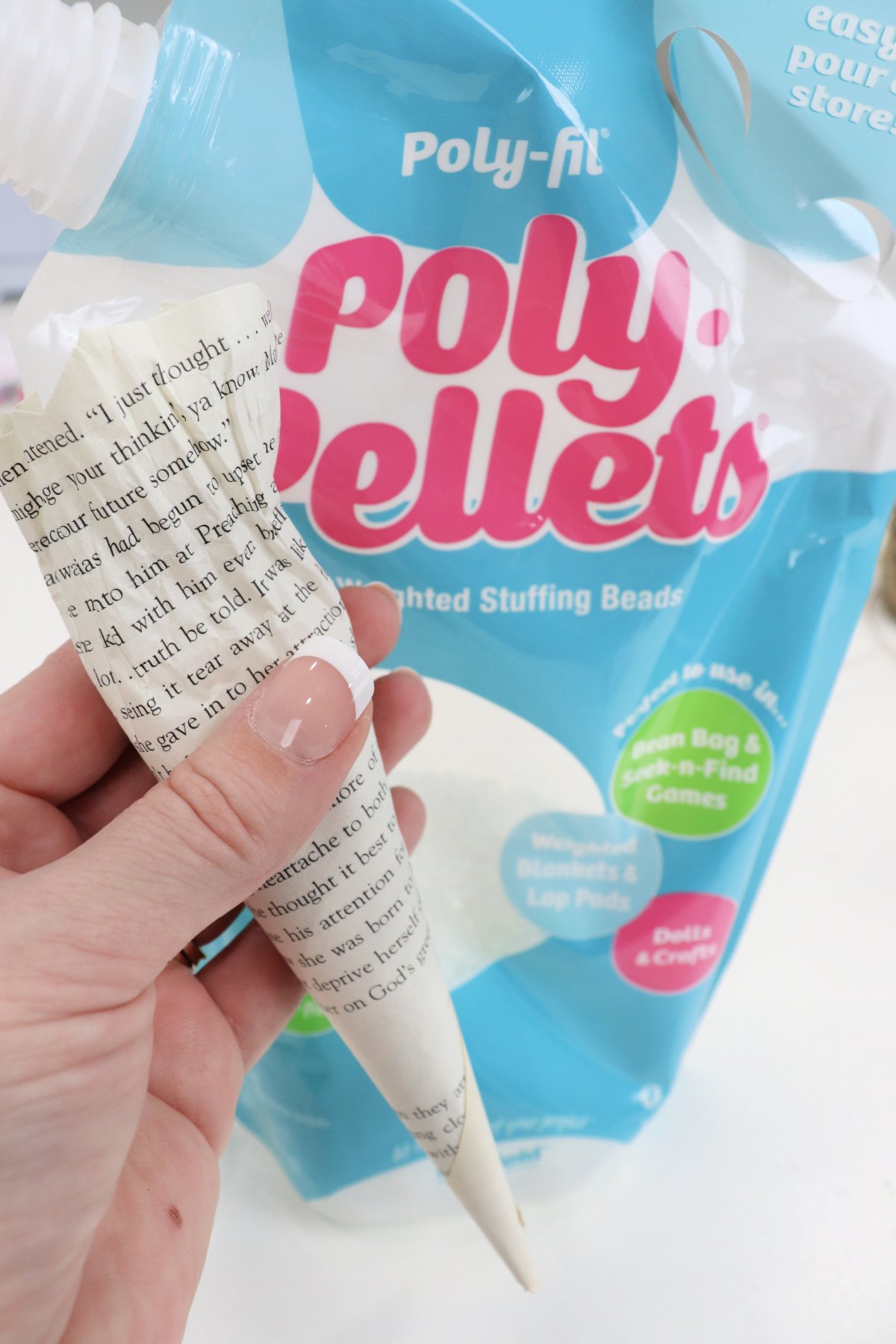 Image contains Amy's hand holding a book page rolled into a cone shape with a bag of Poly-Pellets in the background.