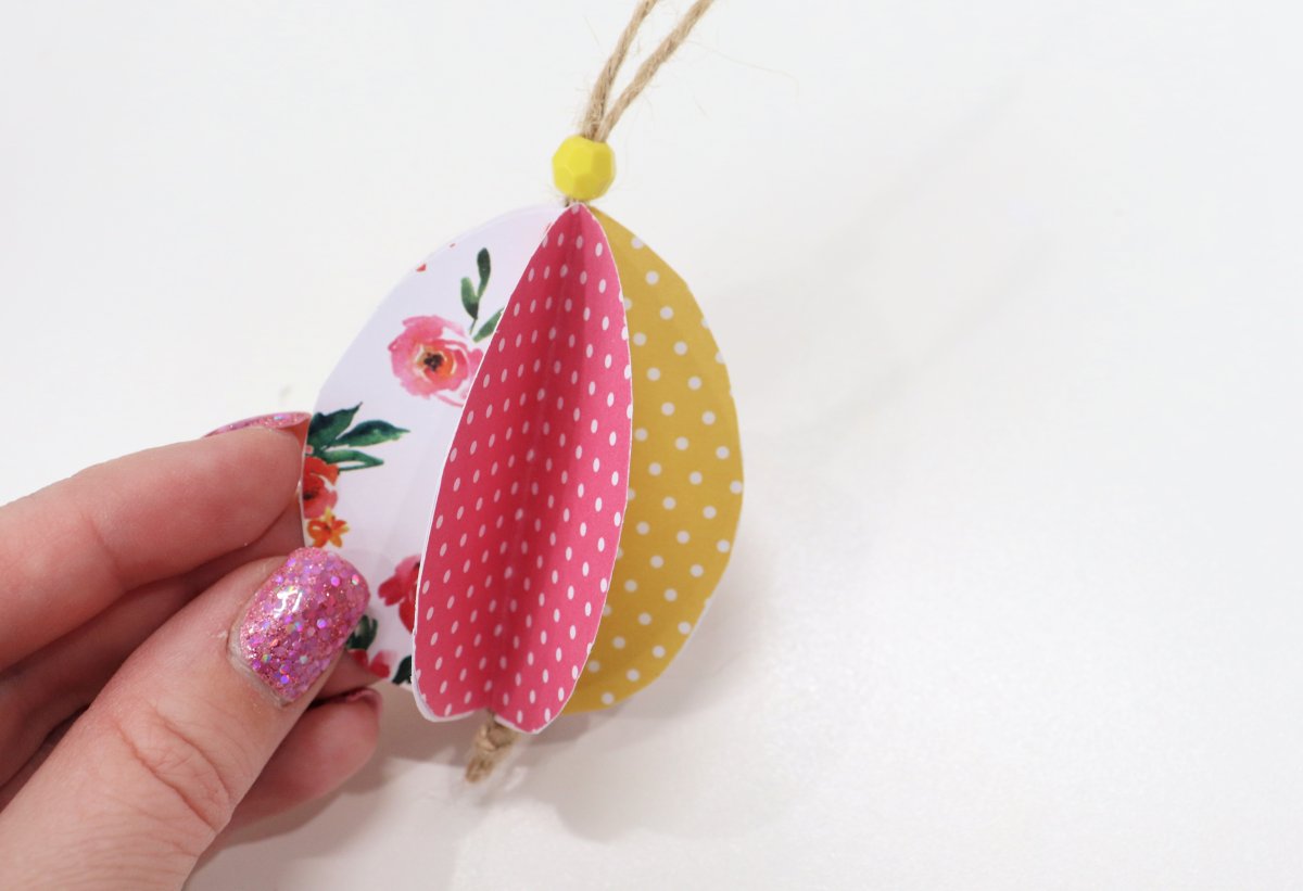 Image contains Amy's hand holding a completed 3-D paper egg made from pink, yellow, and white patterned scrapbook paper.