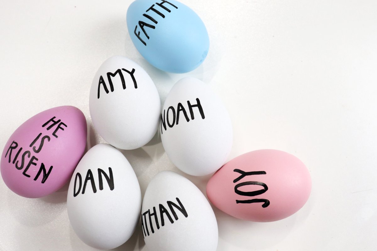 Image contains seven faux eggs; some white, some colored, with names and phrases written in a farmhouse style print.