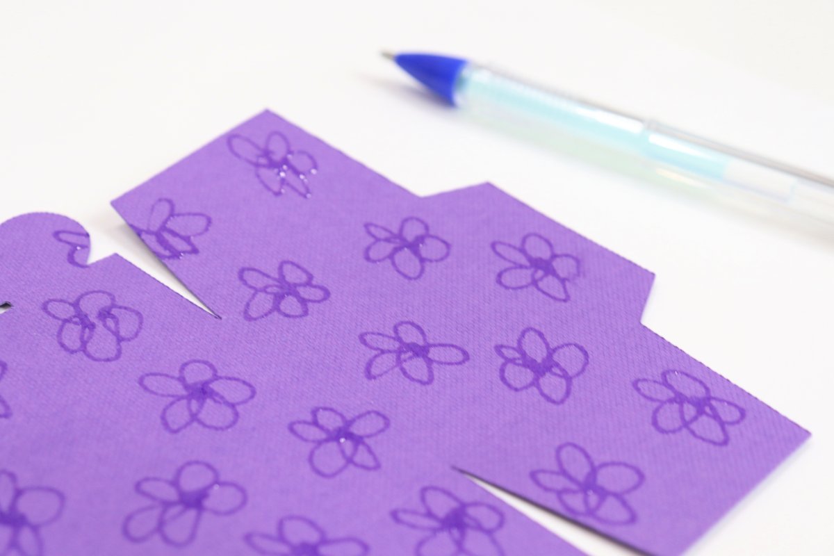 Image contains a close-up of purple cardstock with flowers drawn on it in glue pen. It sits on a white background with the glue pen off to the side.