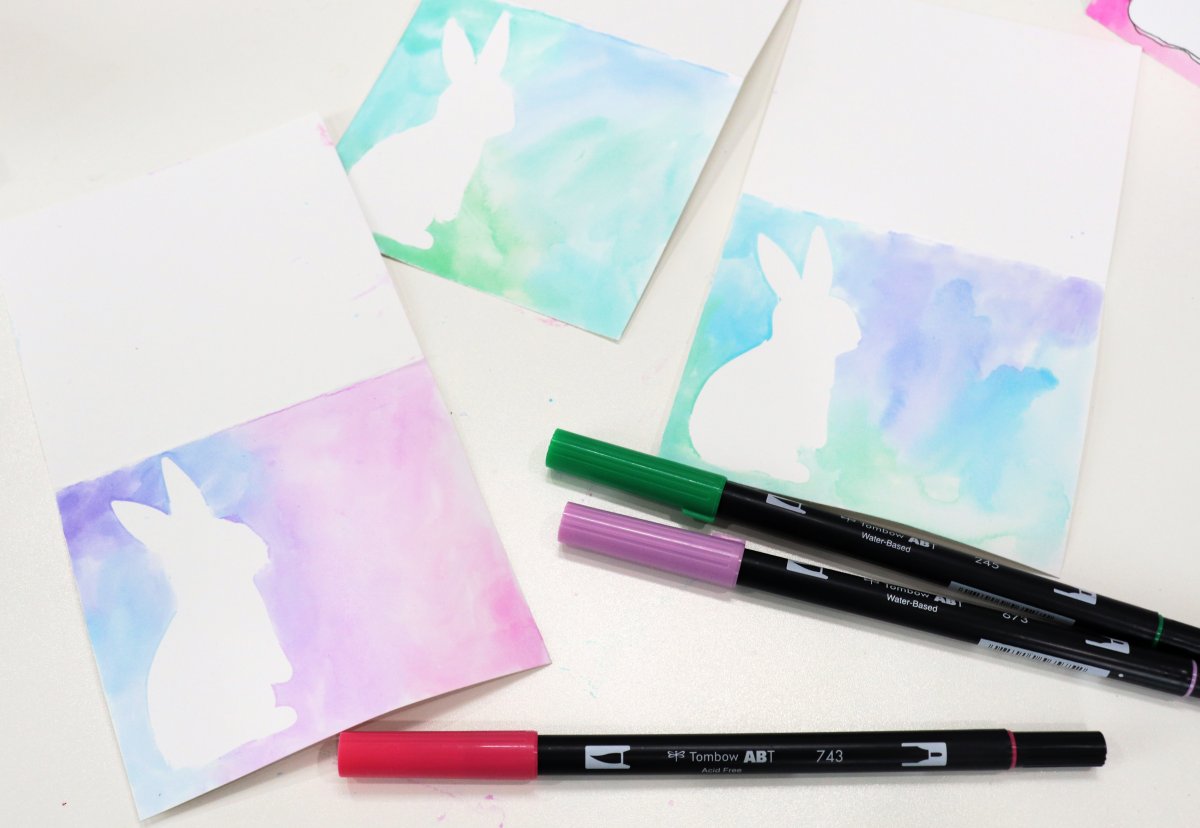 Image contains three placecards with a white bunny on a multi-colored watercolor background. They sit on a white background with three markers.