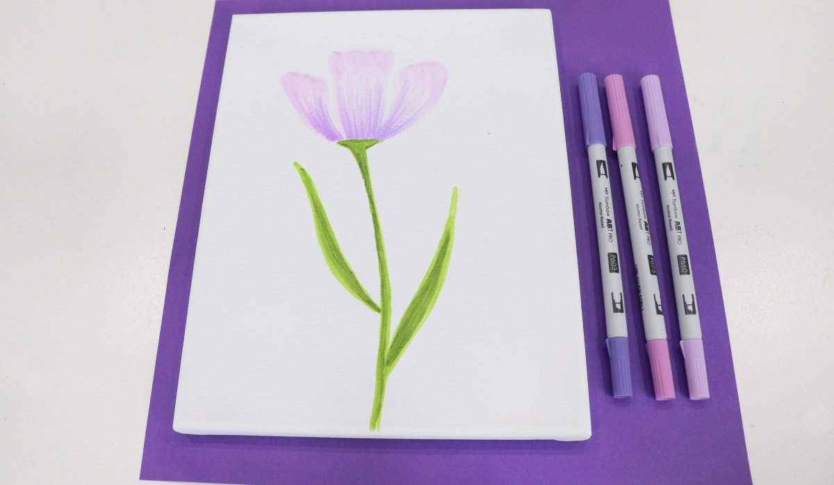 Image contains a white canvas with a three-petaled purple flower drawn on it. Three purple markers sit beside it on a purple background.