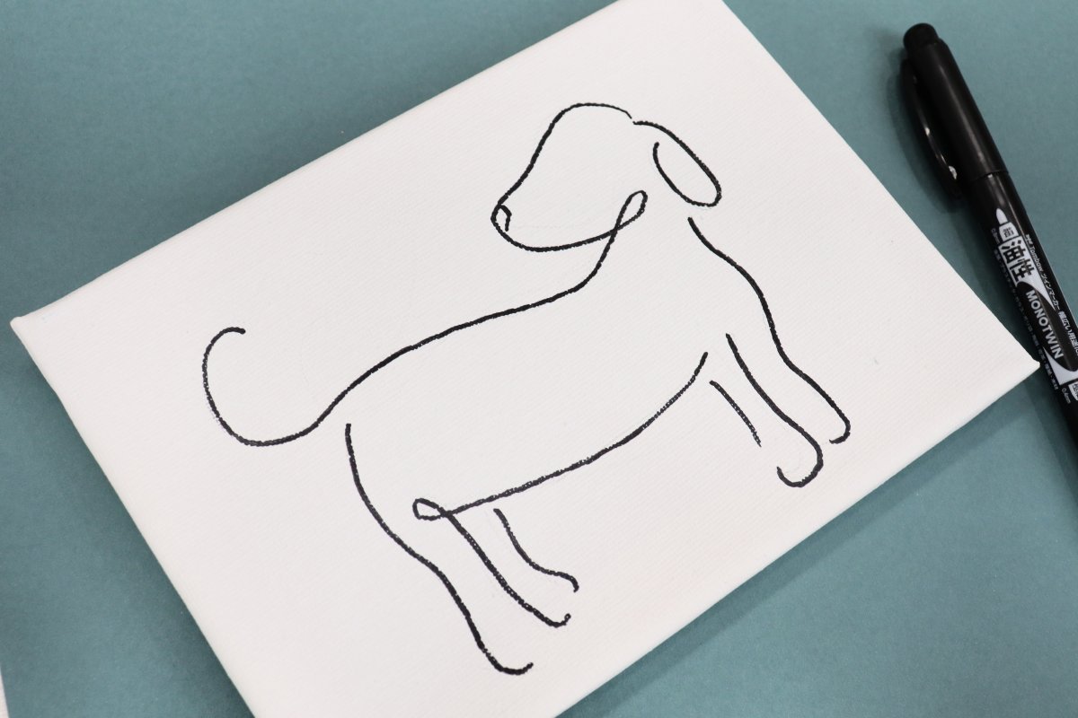 Image contains a white canvas decorated with a line drawing of a dog looking over its shoulder. It sits on a teal background with a black marker.