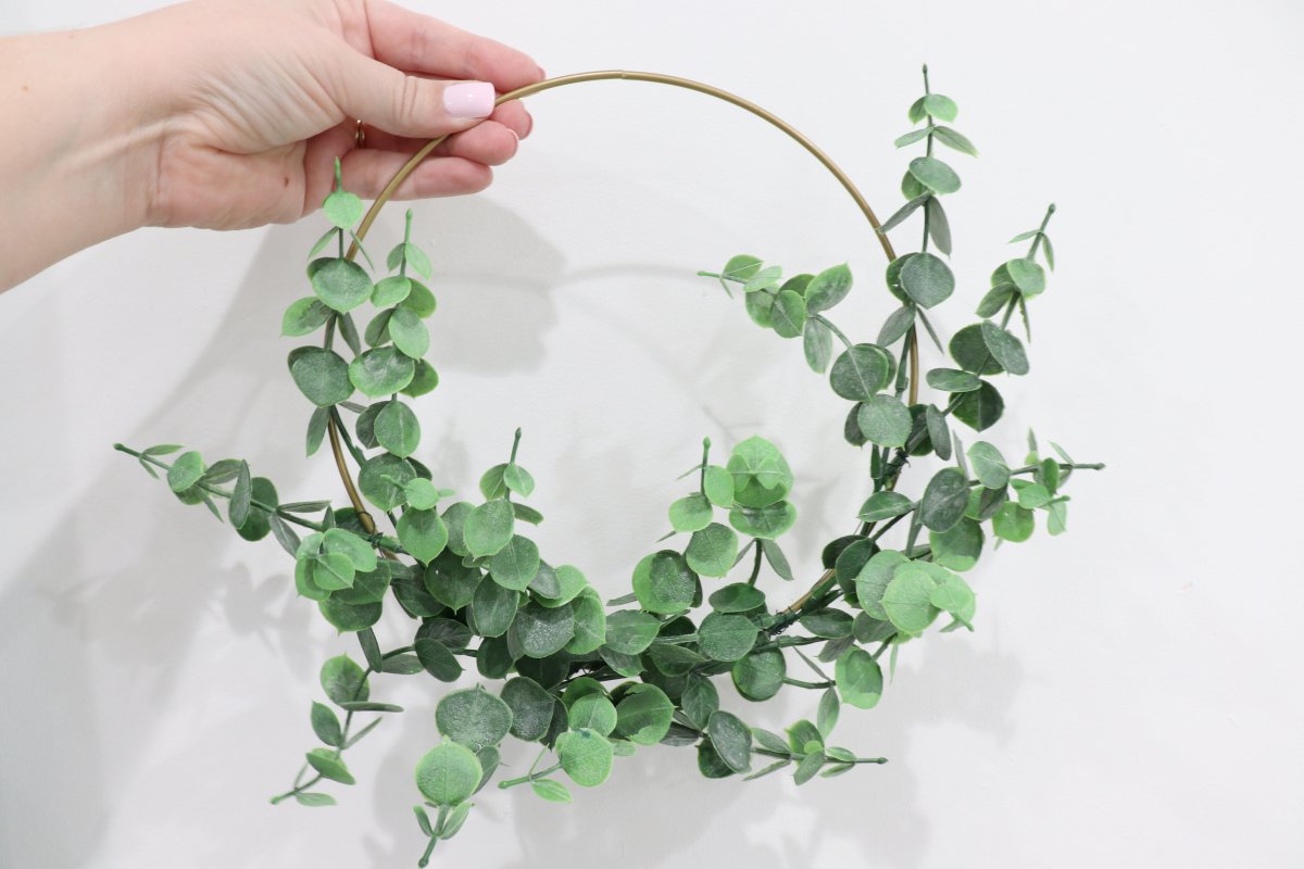 Image contains Amy's hand holding a small wreath made of faux eucalyptus wired onto a gold hoop.