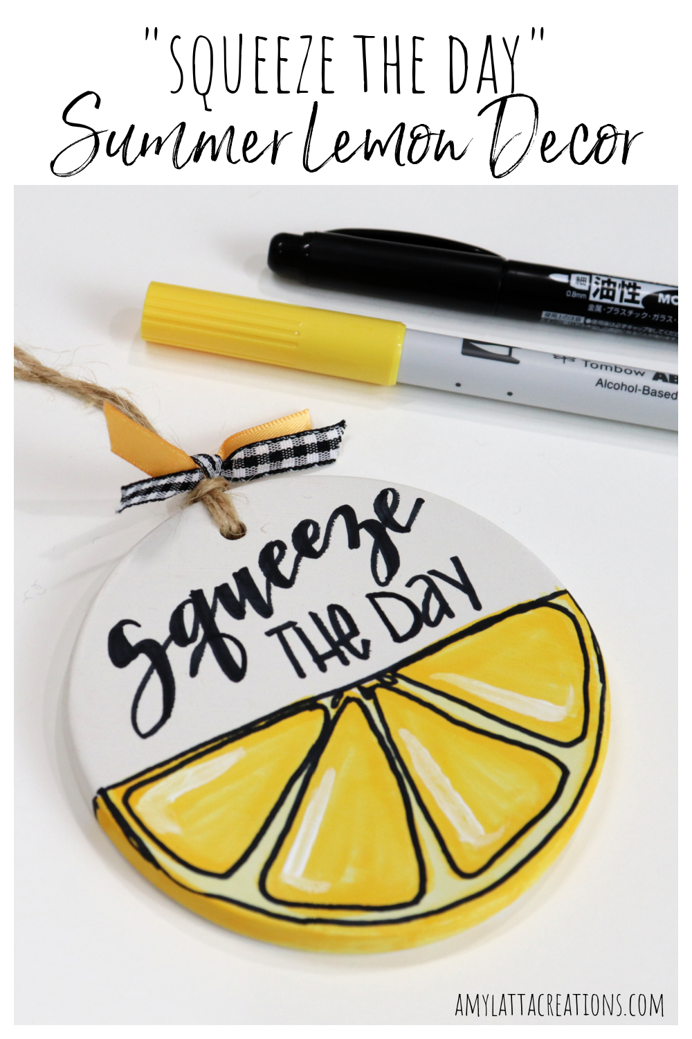 Image is a round, flat white ornament where the bottom half is painted to look like a lemon slice. The words, "Squeeze the day," are written in the top half with black marker. It sits on a white background, next to yellow and black markers.