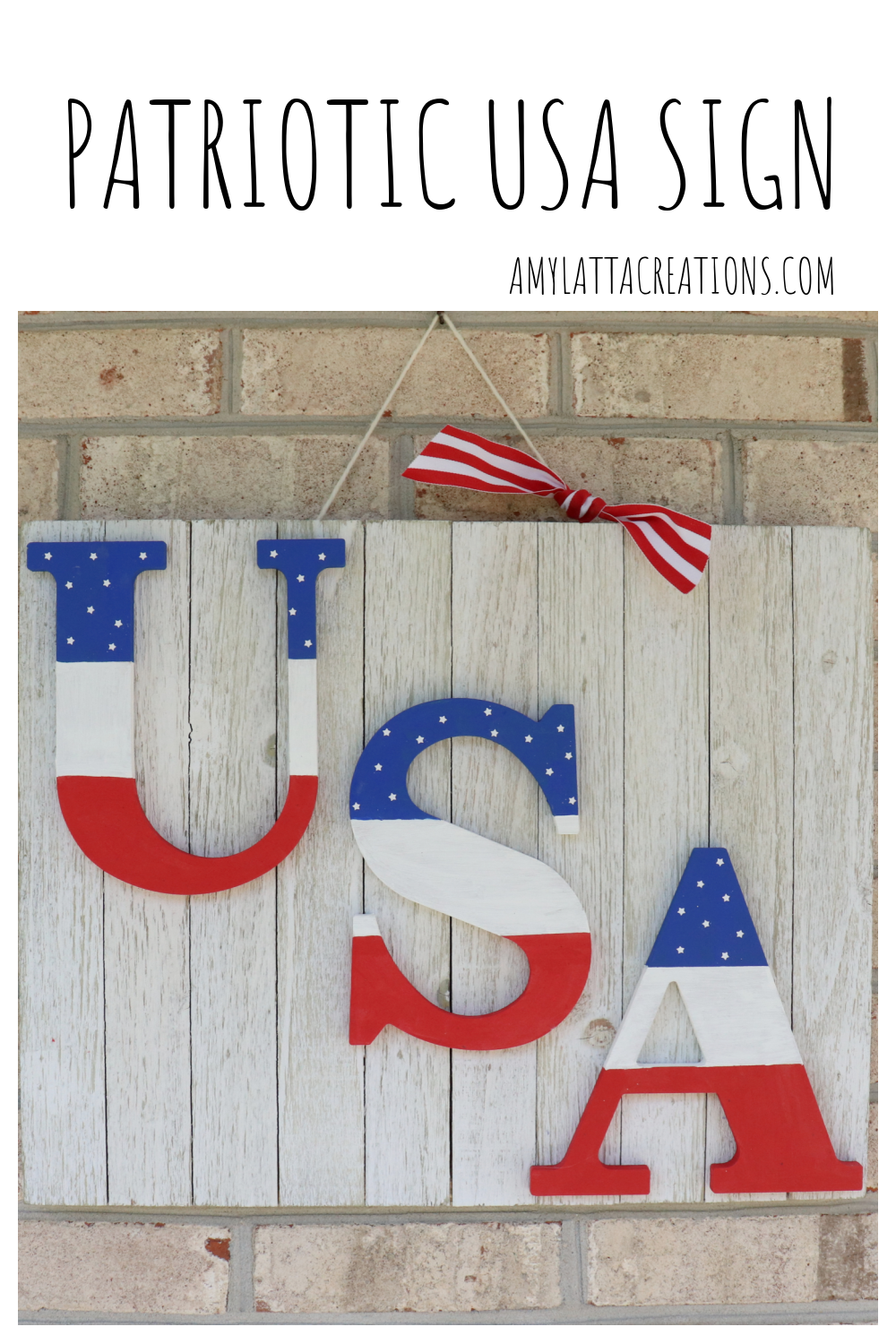 Image contains a white wooden sign with the letters "USA" painted in red, white, and blue. The sign hangs on a brick background.