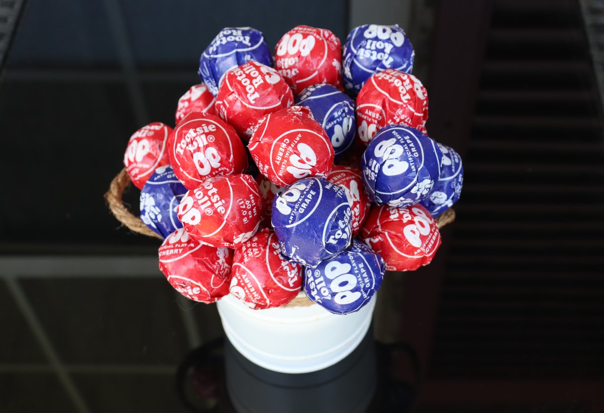Image contains a white bucket filled with red and blue Tootsie Pops on a black background.