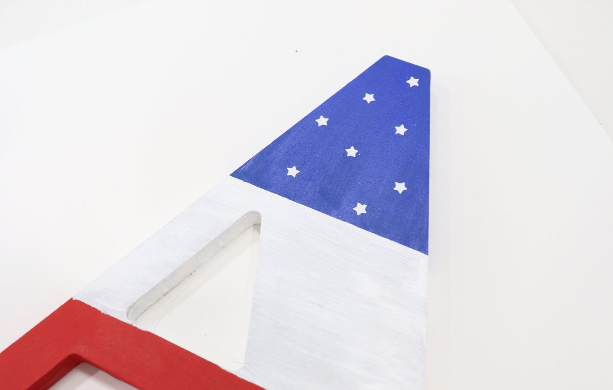 Image contains a wooden letter "A" painted blue, white, and red, with tiny white stars in the blue section.