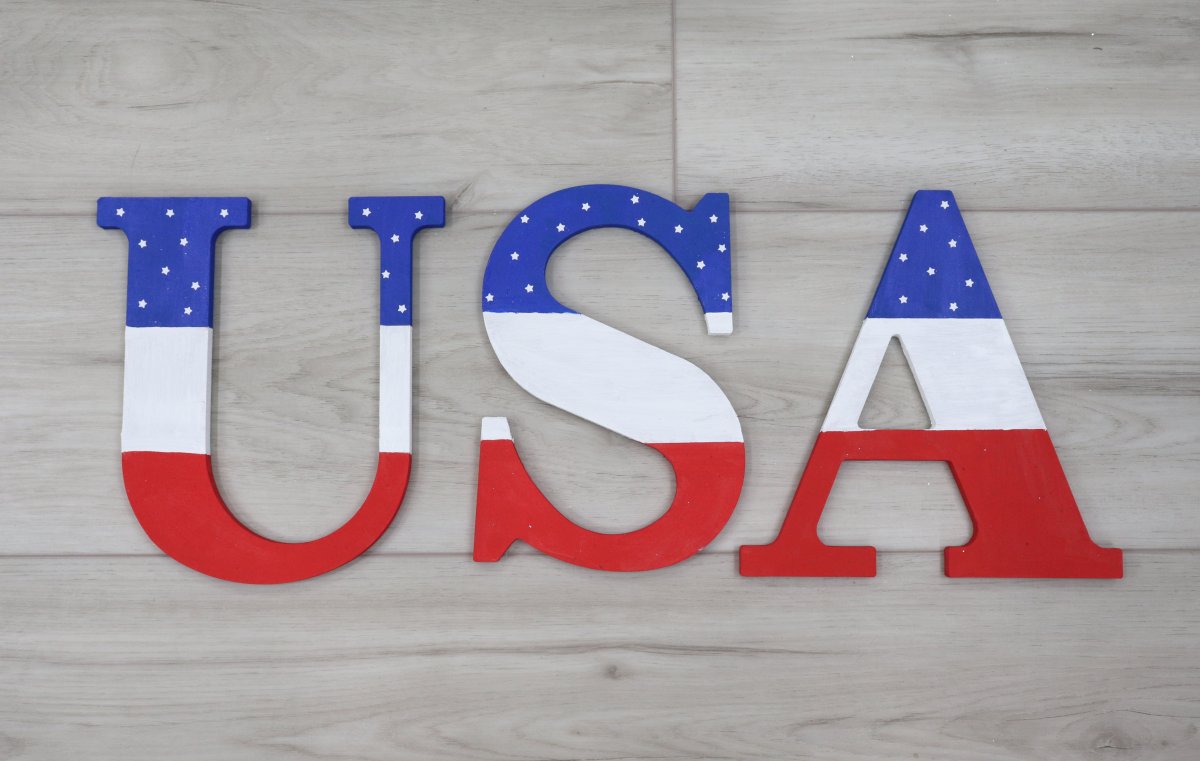 Image contains wooden letters, "USA," painted in red, white, and blue, on a wooden background.