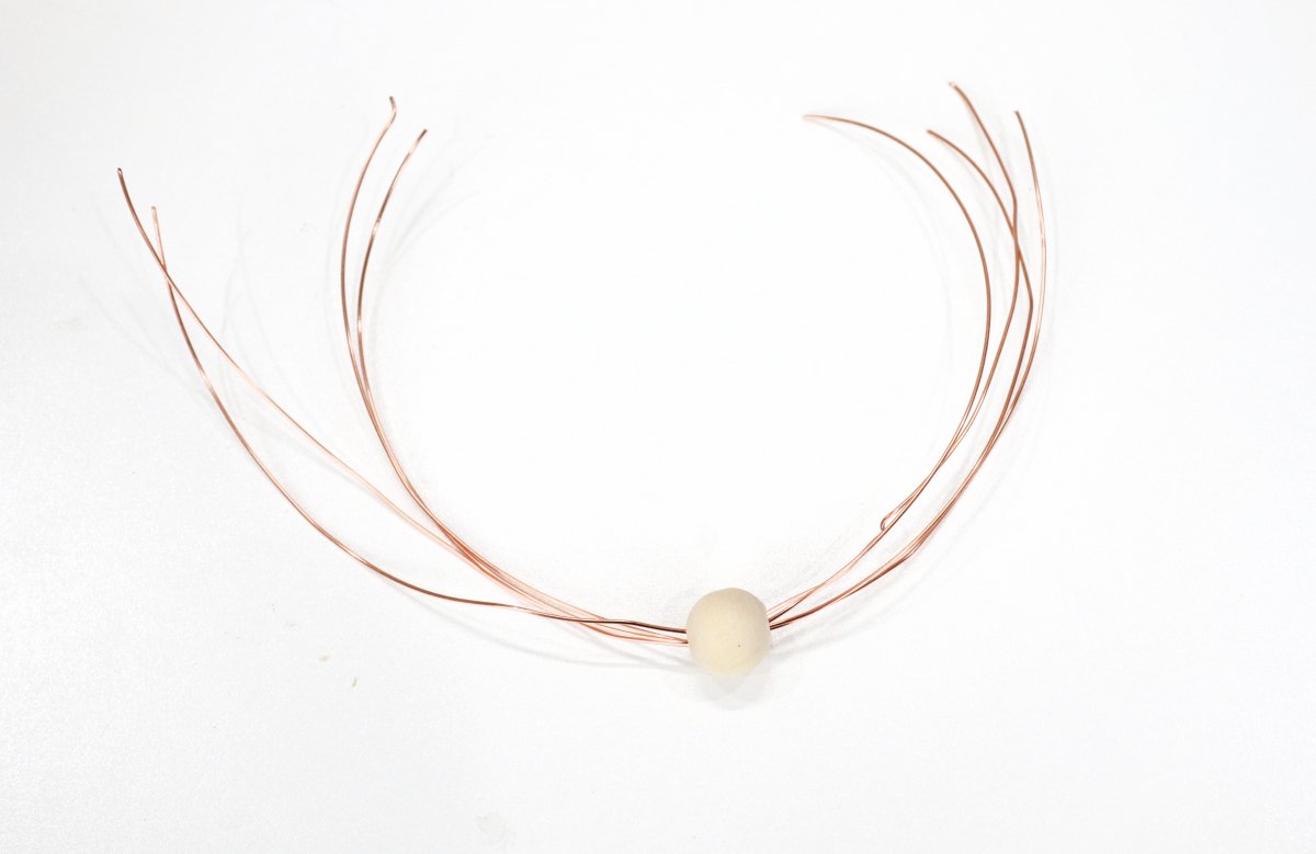 Image contains a wooden bead in the center of four 12" strands of copper wire.