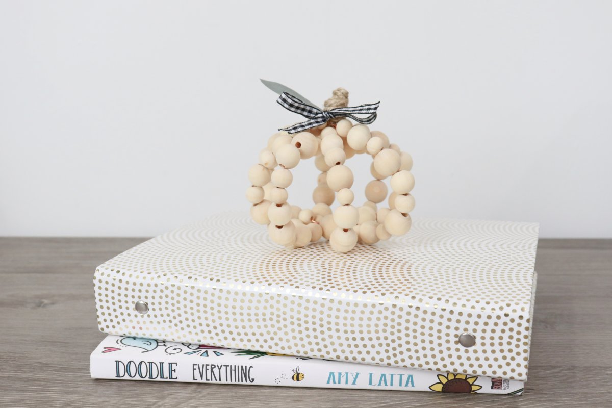 Image contains a pumpkin made of wooden beads sitting on top of books.