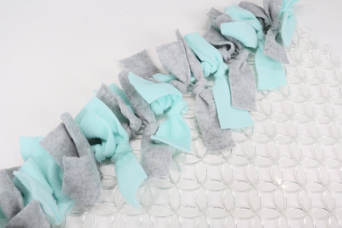 Image contains teal and gray fleece strips tied to a clear rubber kitchen mat.
