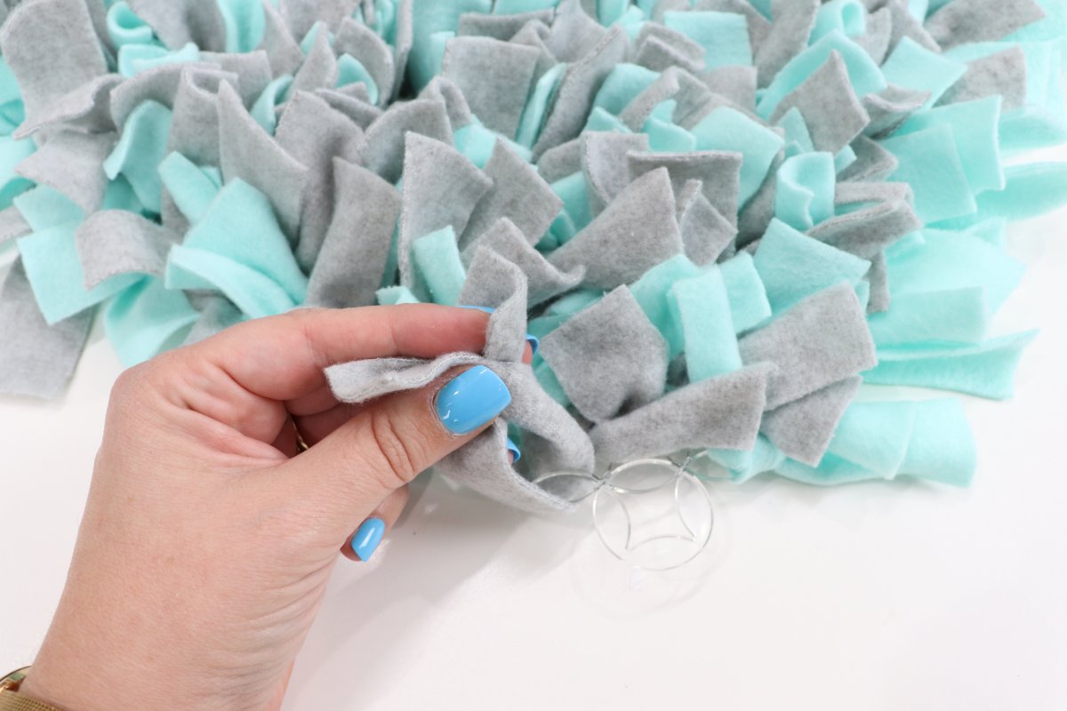 Image contains Amy's hand tying a piece of gray fleece onto a teal and gray snuffle mat.