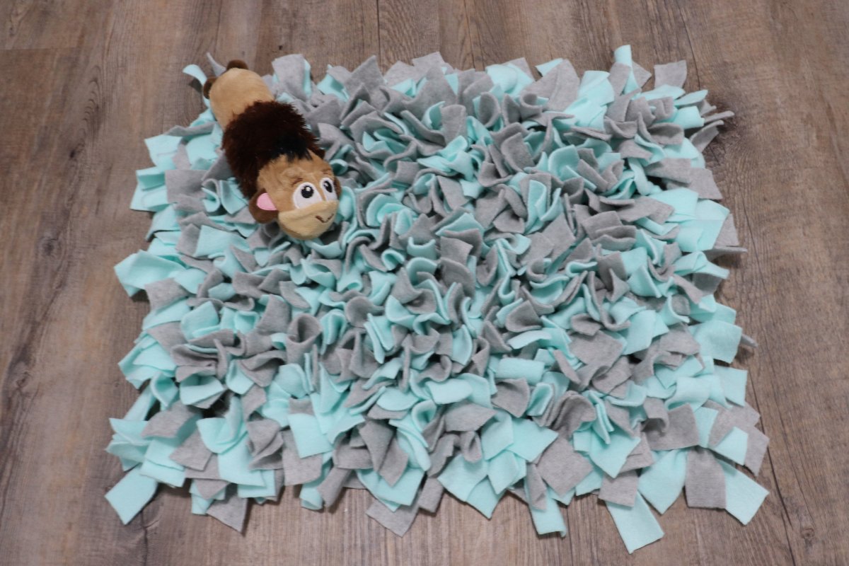 Image is a teal and gray dog snuffle mat with a monkey dog toy on top, sitting on a wood floor.