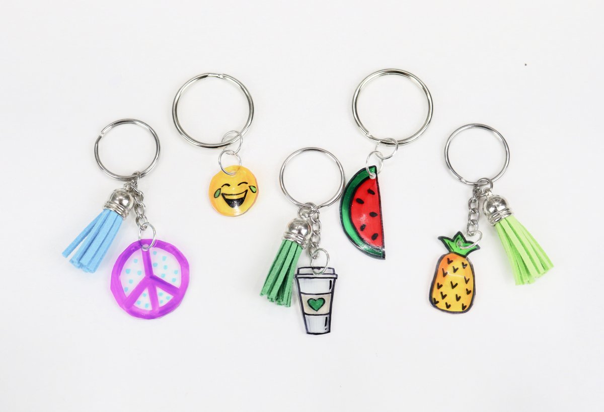Image contains five keychains made with hand-drawn charms; a peace sign, a laughing emoji, a coffee cup, a slice of watermelon, and a pineapple.