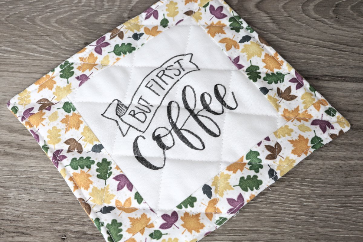 Image contains a quilted coaster that reads, "but first, coffee," and contains autumn leaf print fabric.