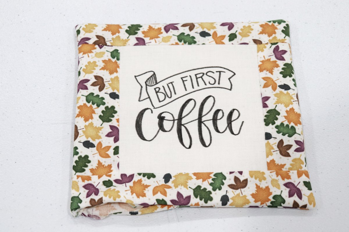 Image contains a quilted coaster in progress; a lettered square surrounded by autumn leaf print fabric.