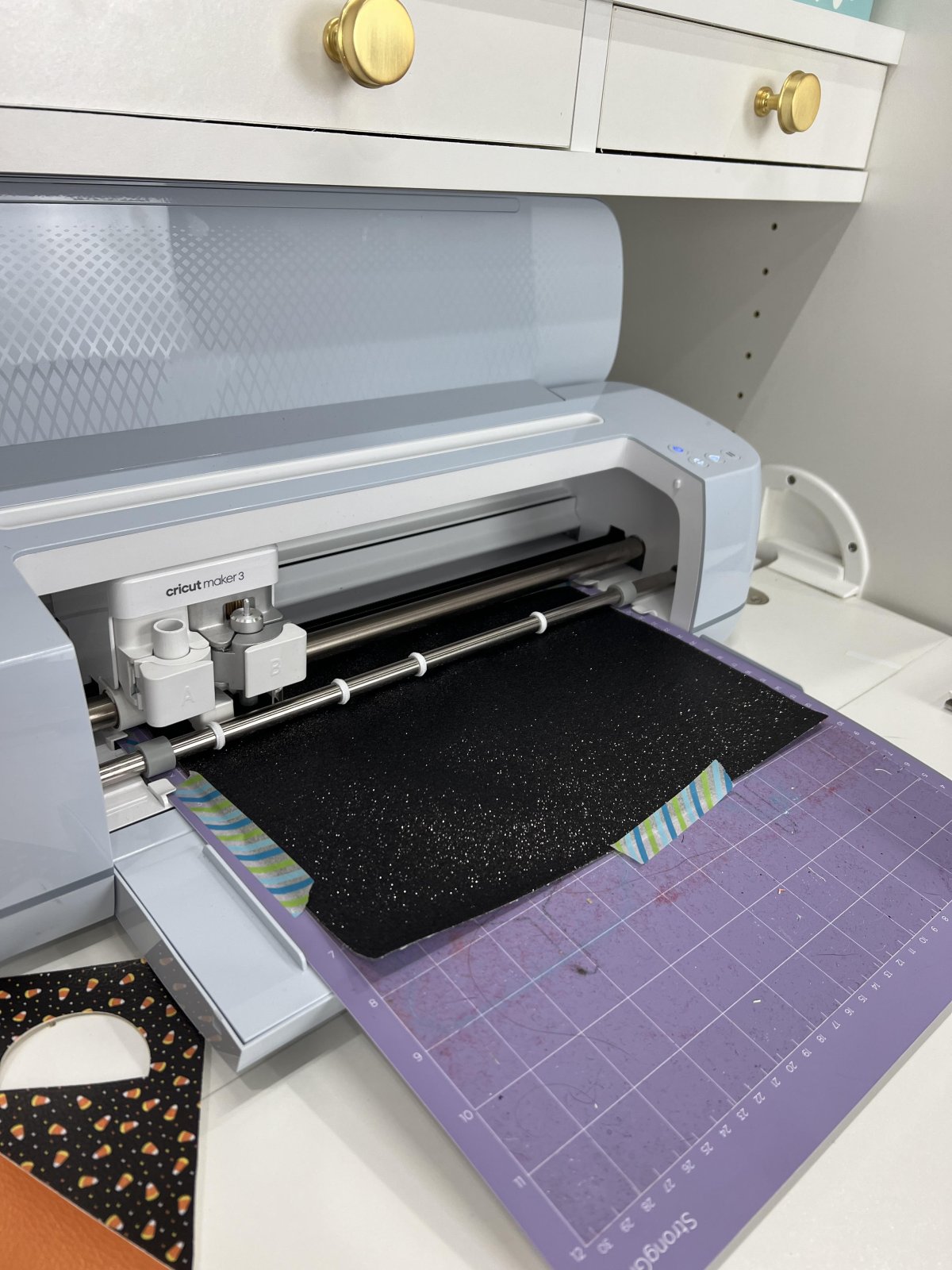 Image shows a Cricut Maker 3 cutting a piece of black faux leather on a purple cutting mat.