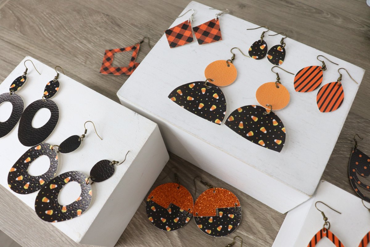 Image contains an assortment of faux leather dangle earrings in a variety of orange and black colors and patterns.